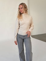 Modelfoto af pige i beige WHITNEY strik, samt grå NANNA jeans. Alt er fra BySofieSønderby.