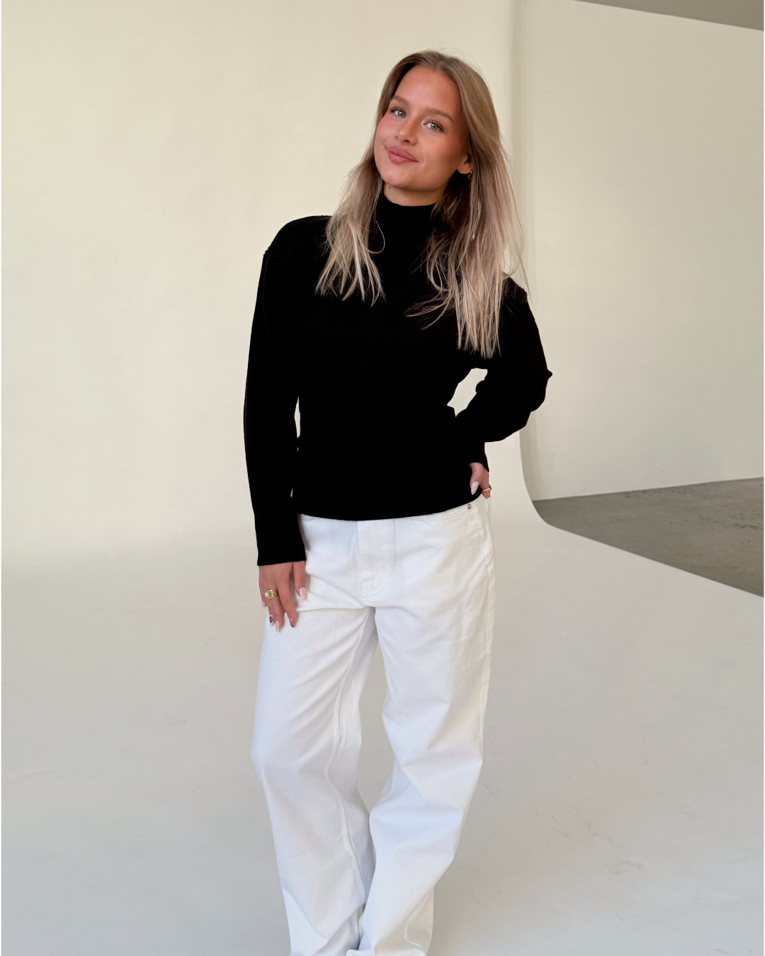 Modelfoto af pige i sort WHITNEY strik, samt hvide NANNA jeans. Alt er fra BySofieSønderby.