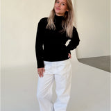 Modelfoto af pige i sort WHITNEY strik, samt hvide NANNA jeans. Alt er fra BySofieSønderby.