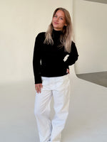 Modelfoto af pige i sort WHITNEY strik, samt hvide NANNA jeans. Alt er fra BySofieSønderby.