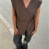 Modelfoto af pige i brun Yui vest med bindebånd, samt grå Nanna jeans. Alt er fra BySofieSønderby